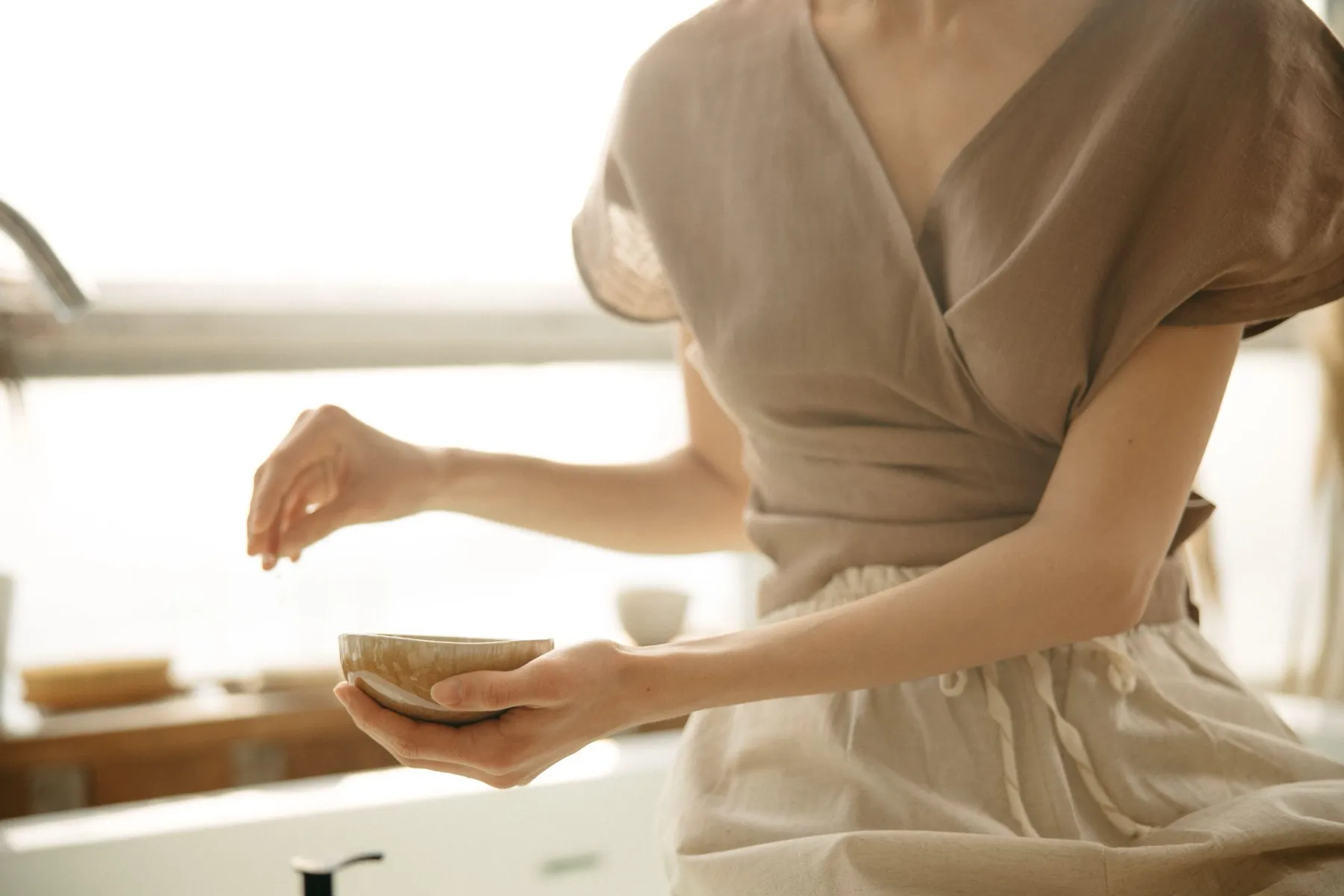 Mujer con ropa de lino en tonos crema sosteniendo un cuenco, con luz natural