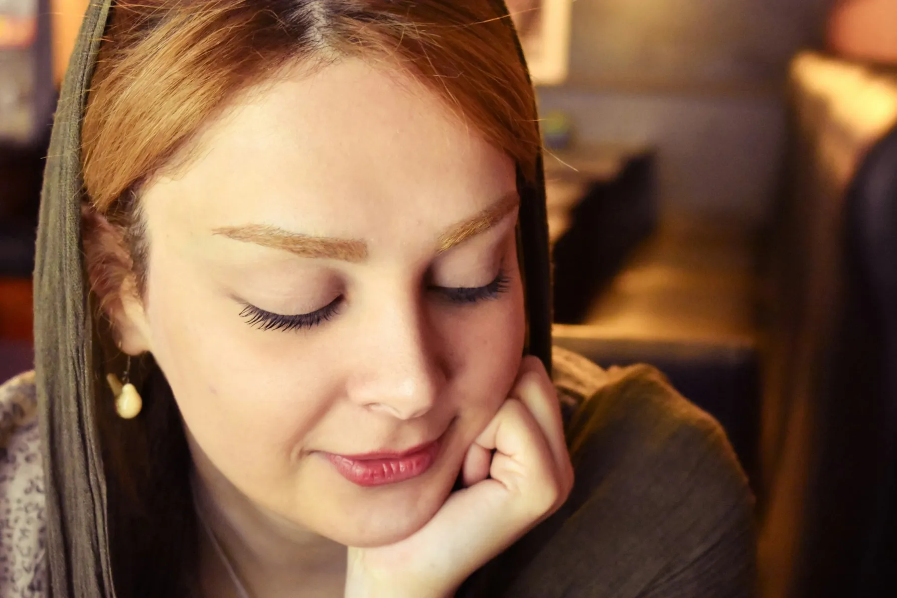 Mujer con los ojos cerrados y la mano junto al rostro, con luz cálida